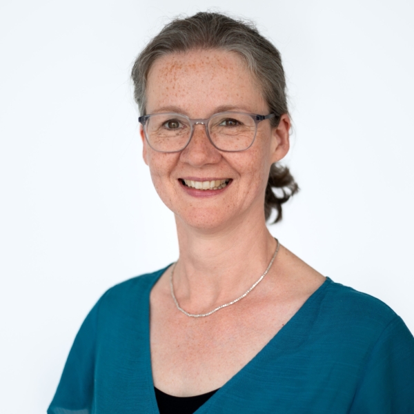 Portrait von Monica Wellmann die ein blaues Oberteil trägt und in die Kamera lächelt