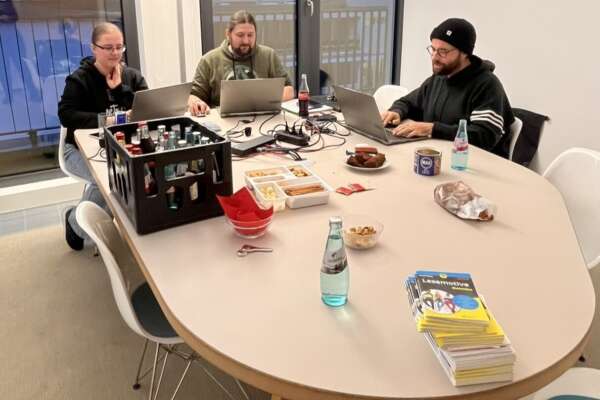 Zwei Männer und eine Frau sitzen mit drei Laptops an einem Tisch. 