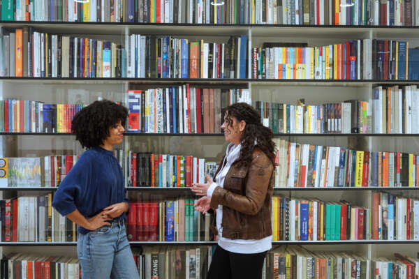 Zwei Frauen reden vor einem Bücherregal miteinander.