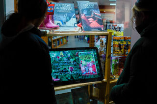 Zwei Frauen sehen sich die Buchwerbung auf einer digitalen Werbetafel an.