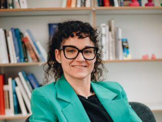 Susanne Breuer sitzt auf einem Stuhl vor einem Bücherregal.