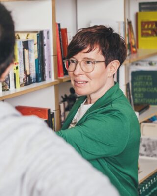Silke erklärt einer Person etwas an einem Regal