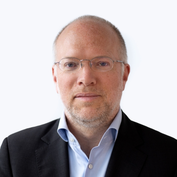 Portrait von Björn Biester. Er lächelt in die Kamera und trägt ein blaues Hemd und ein schwarzes Jacket.