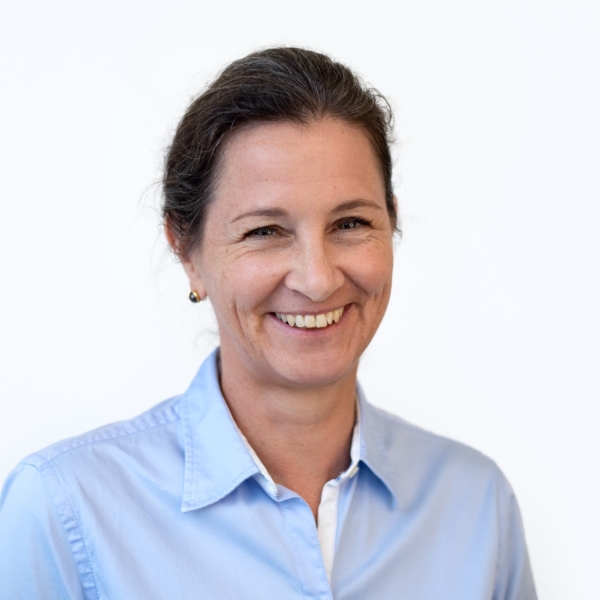Portrait von Katharina Oppitz, die eine blaue Bluse trägt und in die Kamera lächelt.