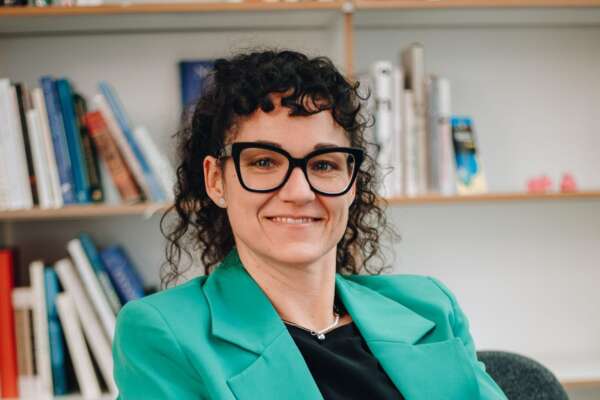 Susanne Breuer sitzt auf einem Stuhl vor einem Bücherregal.