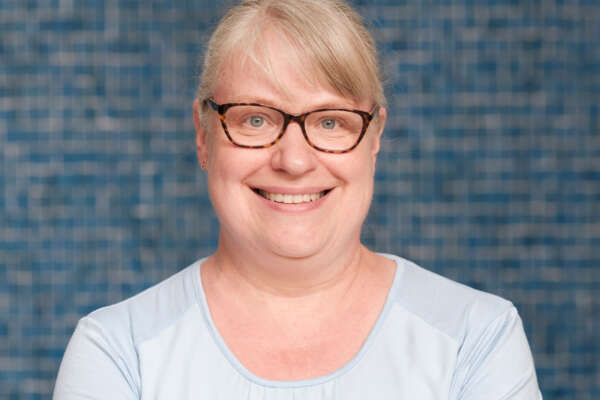 Petra Läufer steht vor einer blauen Wand und lächelt