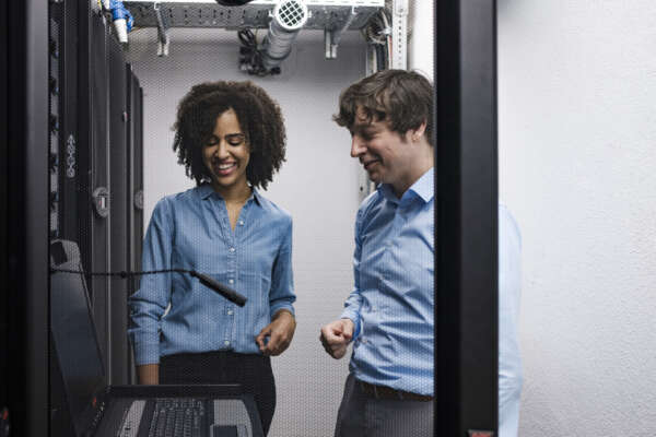 Eine Frau (links) und ein Mann (rechts) stehen in einem Serverraum.