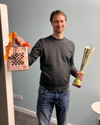 Christian Triebstein lächelt und hält in der linken Hand den Siegerpokal und in der rechten Hand eine Geschenktüte.