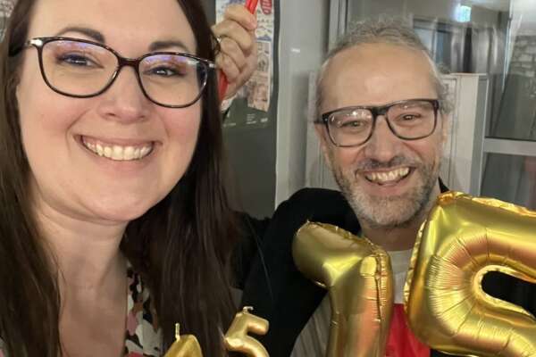 Katrin und Markus lächeln in die Kamera und halten dabei die Zahl 75 in Form von goldenen Kerzen und Ballons.