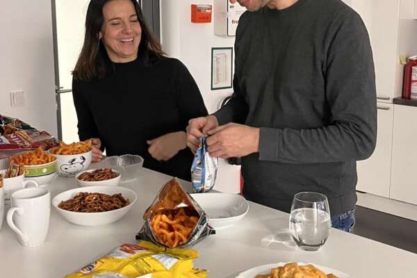 Eine Frau und ein Mann stehen lächelnd an einem Tisch und bereiten Snacks vor.