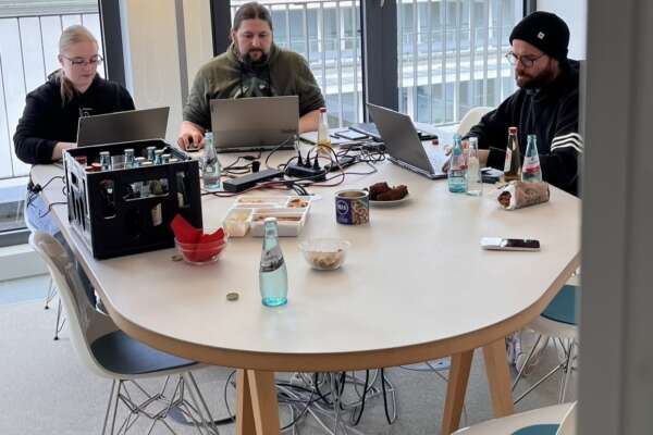 Zwei Männer und eine Frau sitzen mit drei Laptops an einem Tisch.