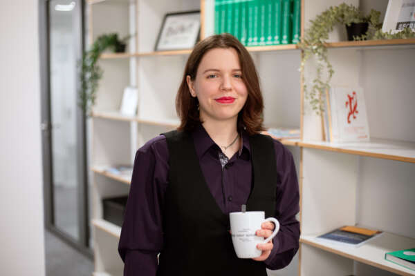  Anna Göckel steht vor einem Bücherregal.