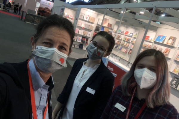 Selfie of Katharina Oppitz, Anna Göckel and another woman in front of a stand at the Frankfurt Book Fair. 