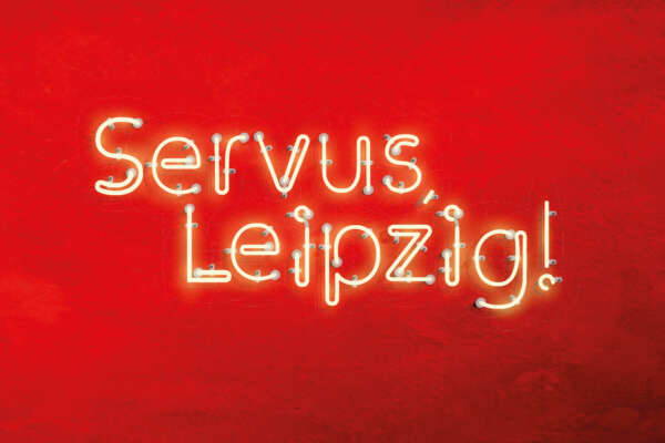 Vor einem roten Hintergrund steht in gelber Schrift "Servus, Leipzig!".