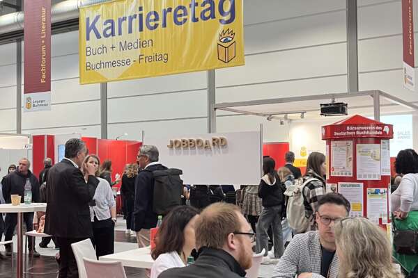 besetzte Tische im Vordergrund, gelbes Karrieretag-Banner im Hintergrund